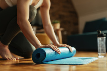 Unrecognizable sportswoman rolling up exercise mat after sports training at home.