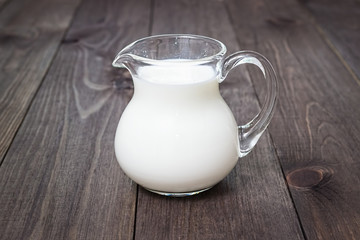 Milk in a glass jug on a wooden background.