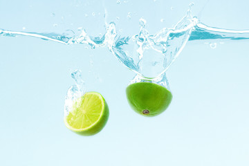 Lime cut into half falling into clean transparent water on blue background