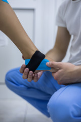 Young man physiotherapist is applying kinesio tape to a patient's leg