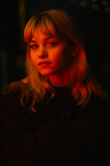 Closeup portrait of a beautiful blonde girl with long curly hair at night with neon lights of the evening city