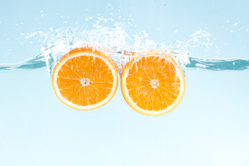Yummy juicy orange cut in half and water splashes on blue background