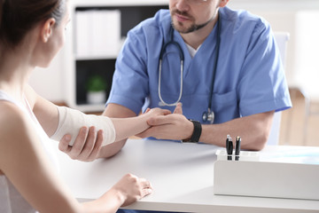 Male orthopedist applying bandage onto patient's elbow at table, closeup