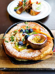 Delicious homemade puff pancake, cooked with vanilla yogurt and fresh fruits, served in vintage red pan on a wooden plate for breakfast
