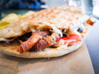 Traditional greek Kebab meat in sandwich prepared with pita bread, cheese and fresh tomatoes and lettuce served in wooden plate with fried potatoes slices.