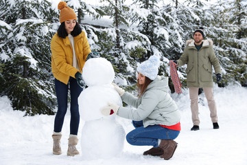 Happy people making snowman together outdoors. Winter vacation
