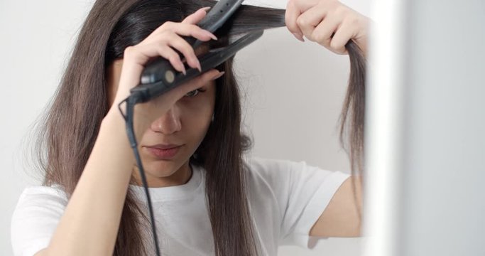 Young attractive brunette lady making hair with iron, beauty routine