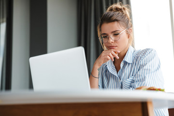 Image of serious nice woman working with laptop while sitting at table