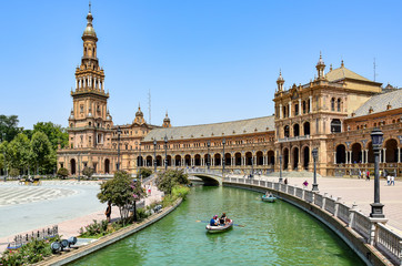 Fototapeta na wymiar Seville, Spain - Square of Spain, a neo-Moorish-style urban ensemble, light brown buildings with numerous arches, people in boats sailing along a channel with greenish water, in the summer afternoon.