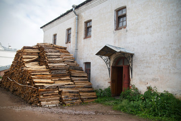 A large pile of firewood lies in the yard near an old house on a summer morning in the countryside.