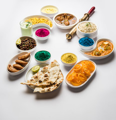 Happy Holy concept  showing Indian assorted lunch food like chicken, paneer butter masala, naan, jeera rice, black chana fry, jalebi, fujiyama, thandai and Farsan with holi colours and pichkari 
