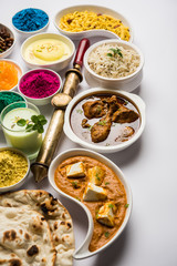 Happy Holy concept  showing Indian assorted lunch food like chicken, paneer butter masala, naan, jeera rice, black chana fry, jalebi, fujiyama, thandai and Farsan with holi colours and pichkari 