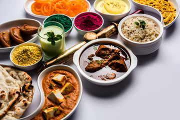 Happy Holy concept  showing Indian assorted lunch food like chicken, paneer butter masala, naan, jeera rice, black chana fry, jalebi, fujiyama, thandai and Farsan with holi colours and pichkari 