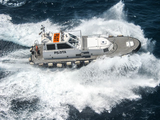pilot boat approaching the big ship before docking viewed from above creating splashes and...