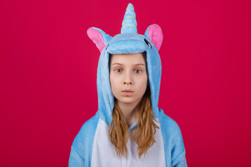 Charming girl playfully poses in the costume of the unicorn. Studio shot of an emotional woman in kigurumi having fun on a pink background.