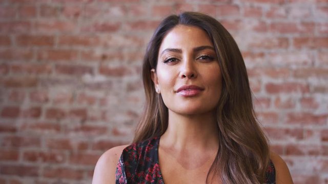 Head and shoulders portrait of smiling Hispanic woman standing against brick wall in coffee shop - shot in slow motion