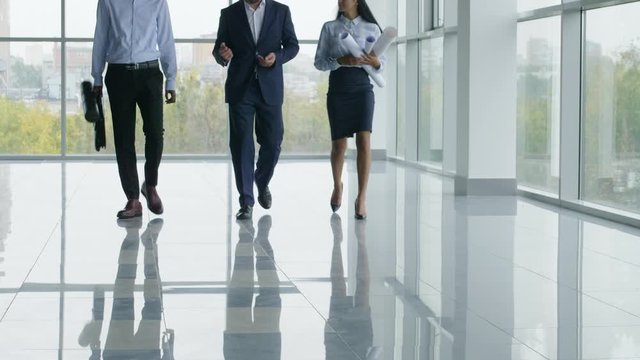 Tilt up shot of Caucasian engineer walking through new modern building and showing exterior to foreign colleagues  