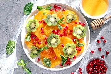 Fruits salad: orange, kiwi, pomegranate and mint served with honey. Top view with copy space. Healthy eating.