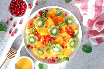 Fruits salad: kiwi, orange, pomegranate and mint served with honey. Healthy eating. Top view with copy space.