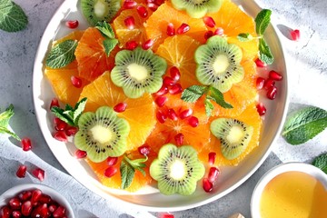 Fruits salad: kiwi, orange, pomegranate and mint served with honey. Healthy eating. Top view with copy space.