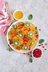 Fruits salad: kiwi, orange, pomegranate and mint served with honey. Healthy eating. Top view with copy space.