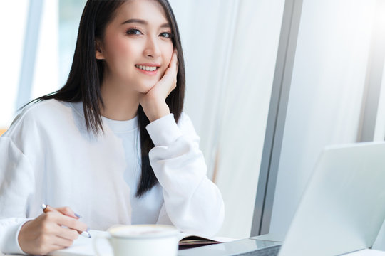 entrepreneur  startup business owner attractive asian female business woman communication with smartphone and laptop white dress cheerful and smile with confience blur office background