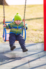 Happy little baby boy swinging on a swing on the playground