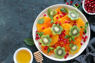 Fruits salad: kiwi, orange, pomegranate and mint served with honey. Healthy eating. Top view with copy space.