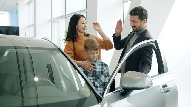 Mother, father and son are buying car doing high-five smiling enjoying new auto in showroom. Positive emotions, modern family and business concept.