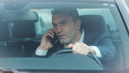 Close up view of handsome man in luxurious car impatiently beeping car horn while not moving in the traffic jam, then angrily talking on the phone and actively waving his arms. Stress, trouble - obrazy, fototapety, plakaty