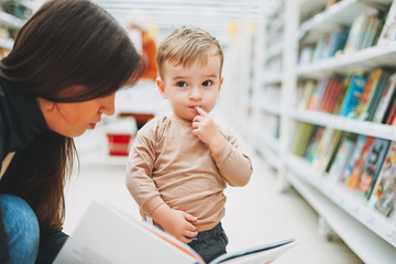Cute baby boy toddler child in bookstore with his mother with open book