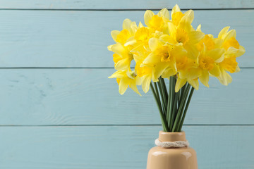 Spring flowers, yellow daffodils in a vase on a blue wooden background. place for text