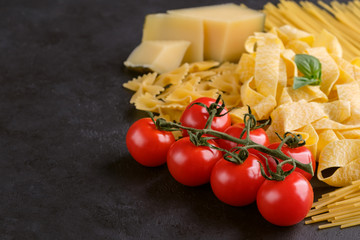 Food background with different types of pasta, tomatoes and parmesan cheese on black stone background. Concept of italian food