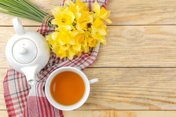 Spring flowers, yellow daffodils and a cup of tea on a natural wooden background. place for text
