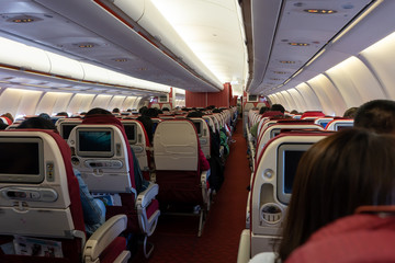 Passenger seat, Interior of airplane with passengers sitting on seats and stewardess walking the aisle in background.