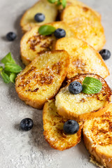 Torrijas, typical Spanish sweet fried toasts with blueberries, coconut flakes and mint on a light grey stone background. Traditional dessert for Lent and Easter. Top view.
