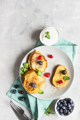 Delicious French toasts with blueberries, dried cherries and mint, light grey background. Sweet breakfast. Top view.