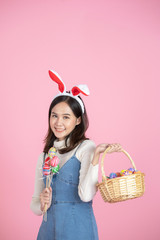 Asian young woman wearing bunny ears showing colorful easter eggs, smiling happy face on pink color background with copy space. Holidays and people concept.