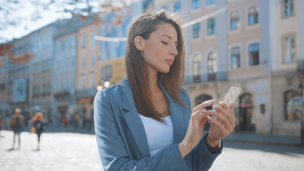 Attractive young woman uses a futuristic glass nanosmartphone holographic technology on street outdoors internet mobile display telephone city portrait modern innovation slow motion