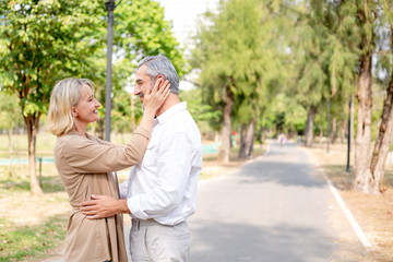 Happy romantic Caucasian couple in love at park, wife hand touching husband face and he wrapping around her, they gazing into eyes, retirement insurance banner for Valentine or anniversary concept