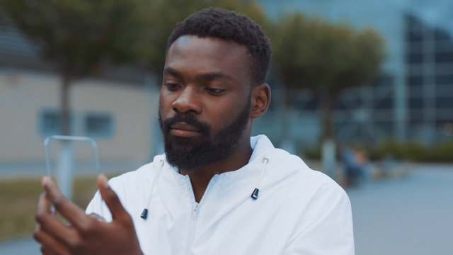 Smiling african american man uses futuristic glass phone walk at city look at camera smile nanosmartphone transparent electronic future global information innovation interface touch web slow motion