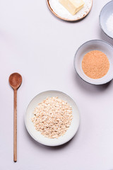 Ingredients for oat porridge: rolled oats or flakes, sugar, salt, milk and butter in a bowls on grey concrete background. Healthy eating, vegetarian food concept. Top view. Selective focus