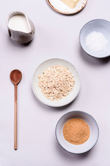 Ingredients for oat porridge: rolled oats or flakes, sugar, salt, milk and butter in a bowls on grey concrete background. Healthy eating, vegetarian food concept. Top view. Selective focus