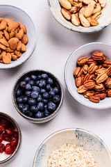 Ingredients for homemade granola: oatmeal, dried cherry, pecans, almond, brazilan nuts, blueberries in a bowls on grey concrete background. Healthy diet breakfast. Flatlay. Top view. Selective focus