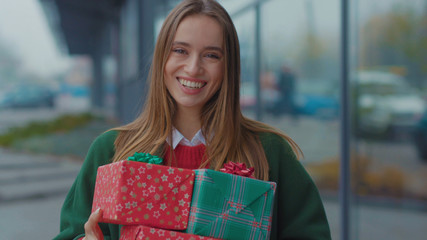 Portrait young woman stand hold Christmas presents gift boxes look at camera smile happy outdoors store winter girl city christmas time tree holiday shopping package attractive close up slow motion