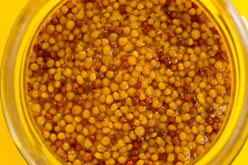 French mustard in a glass jar, shot on a yellow background. Background for seasoning and nutrition.