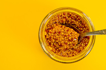 French mustard in a glass jar, shot on a yellow background. Background for seasoning and nutrition.