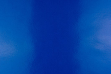 Blue background of real, shiny colored paper, illuminated by a soft light on the sides.