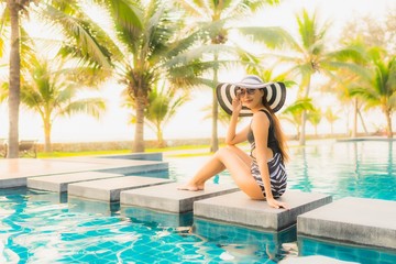 Portrait beautiful young asian woman relax around outdoor swimming pool in hotel resort with palm tree at sunset or sunrise