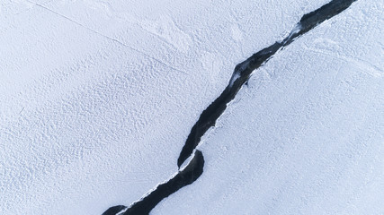 Huge cracks in ice. Textured white snow surface. Winter season.